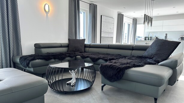 Una sala moderna con un sofá seccional gris, una mesa de centro redonda y un plaid suave negro.