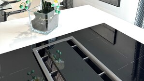 Una cocina moderna con encimera blanca, un florero de vidrio con orquídeas blancas y un lavamanos negro.