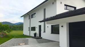 Una casa moderna de dos pisos con fachada blanca, techo negro y un camino de entrada que lleva a un garaje.