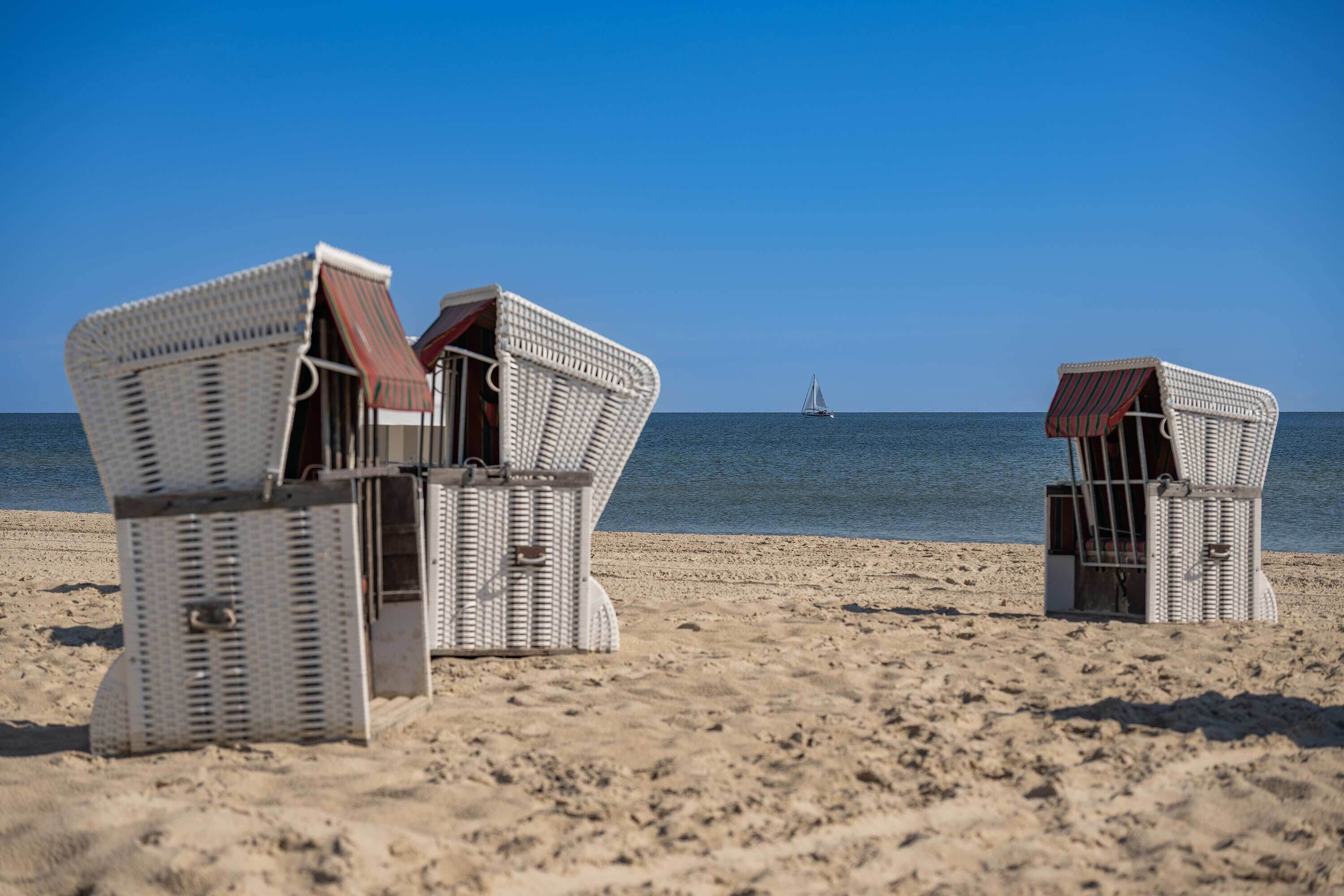 Des fauteuils de plage en osier offrant une vue sur la mer et un voilier au loin.