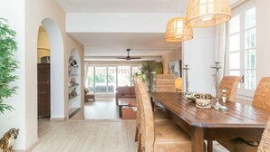 Un comedor amplio con una mesa y sillas de madera, ventanas grandes y un ventilador de techo.