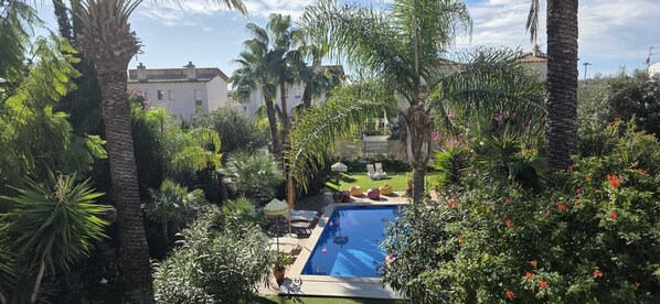 Una piscina rodeada de exuberante follaje y palmeras, con un cielo azul despejado.