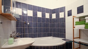 Une salle de bain avec un lavabo blanc, une baignoire et des étagères où sont rangées les serviettes.