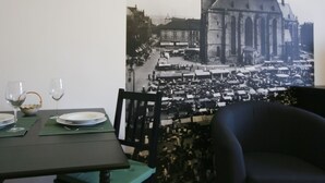 Un coin repas avec une table dressée pour deux personnes, une chaise noire et une grande photographie en noir et blanc représentant un bâtiment historique.