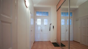Un couloir aux portes blanches, doté d’un sol carrelé et d’un grand miroir qui reflète la pièce.