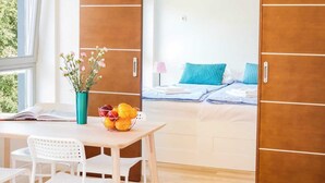 Een kamer met een bed, een tafel met stoelen, een vaas met bloemen en een schaal fruit.