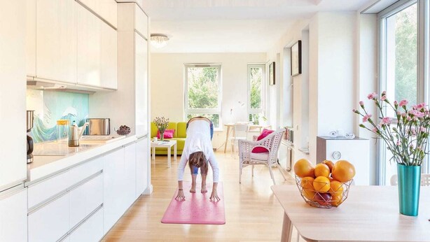 Een ruime kamer met een yogamat, een eettafel met een schaal fruit en een bank.