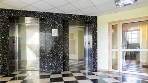 A lobby with a checkered floor, marble walls, and glass doors leading to elevators.