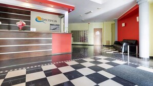 A hotel reception area with a checkered floor, a reception desk, and a seating area with a red wall and a black couch.