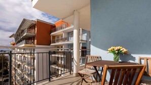 A balcony with a wooden table and chairs, a vase of flowers, and a view of adjacent buildings.