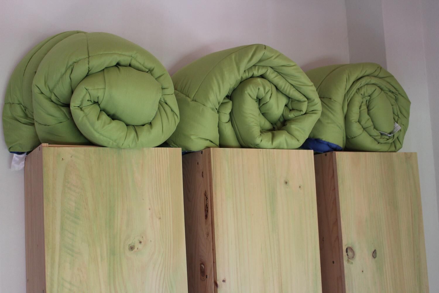 Three rolled green cushions stacked on wooden cabinets.