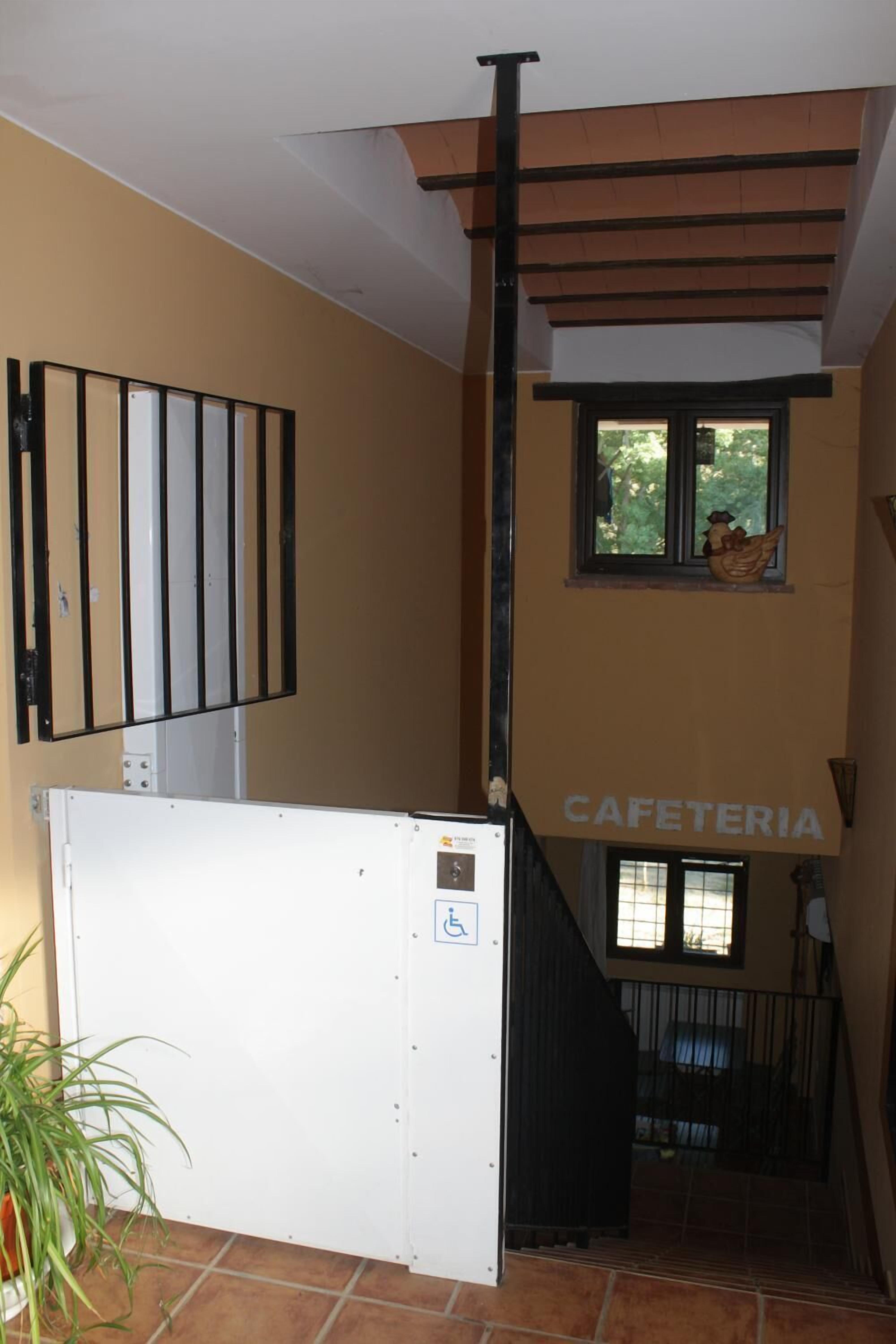 Una escalera con barandilla, una puerta blanca con el símbolo de accesibilidad para sillas de ruedas y una ventana decorada con un gallo.
