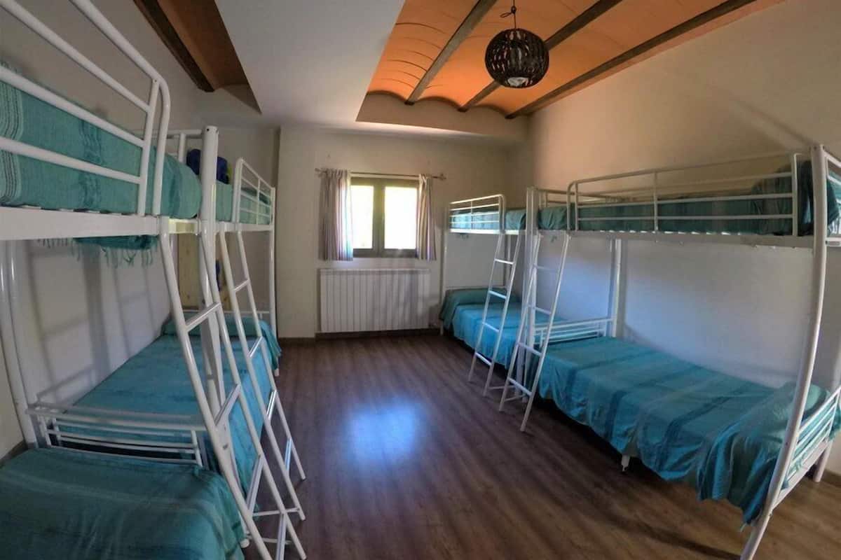 Un dormitorio con literas, una ventana con cortinas, un radiador y una lámpara colgante.