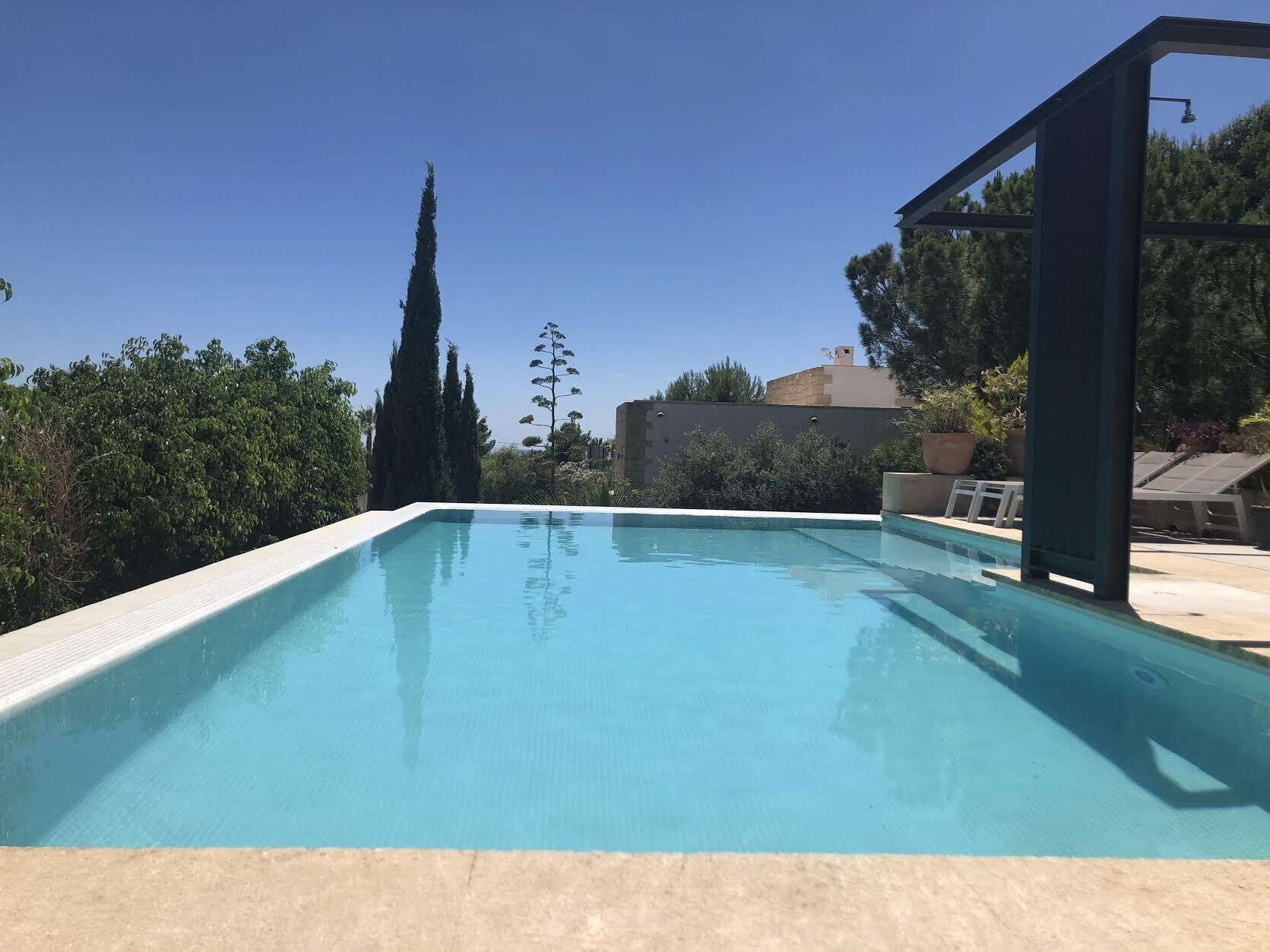 Une piscine rectangulaire à l’eau d’un bleu limpide, entourée de verdure et bordée d’un ciel dégagé.