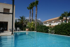 Una piscina con sillas de descanso, palmeras y una montaña al fondo.