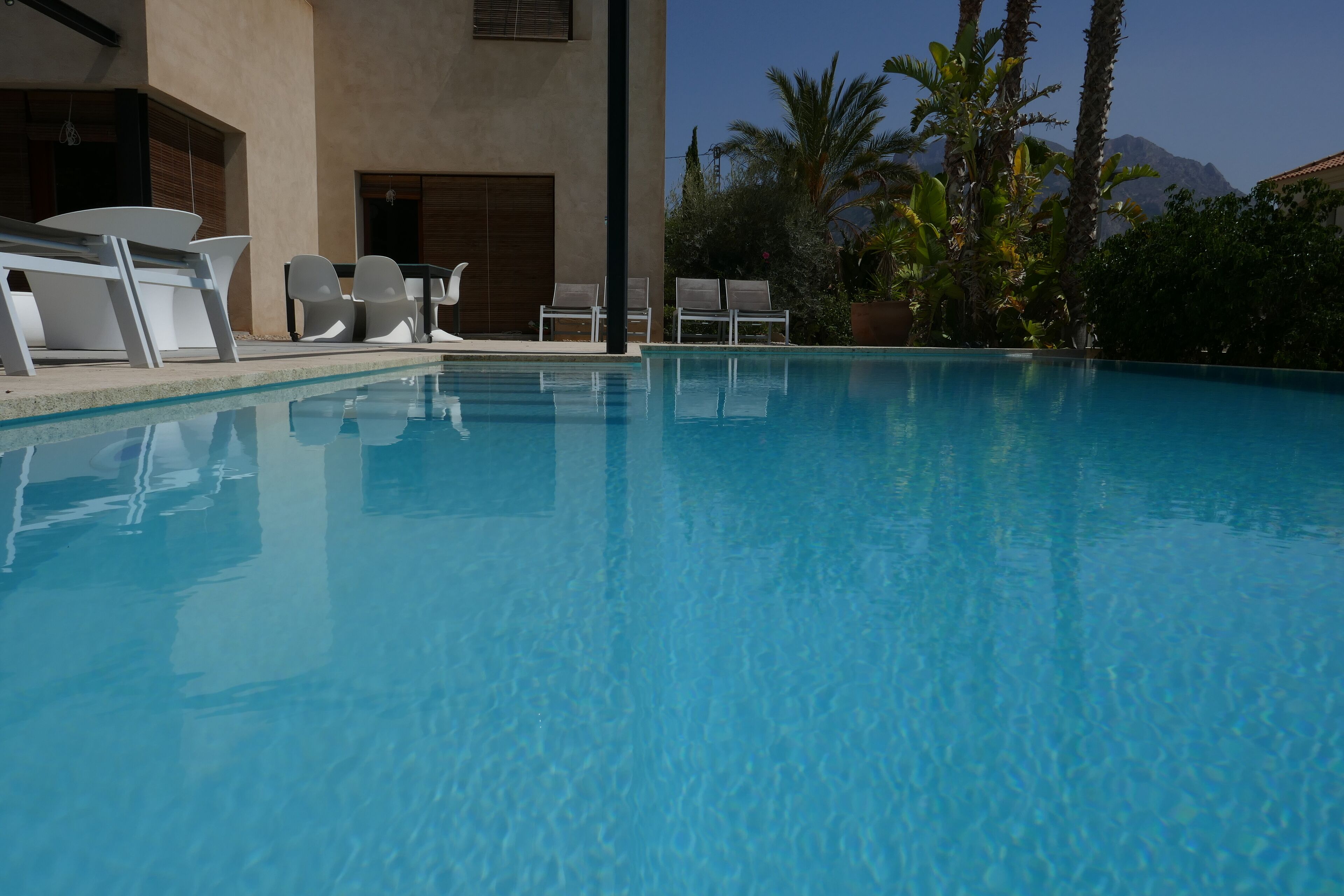 Une piscine d’un bleu éclatant, avec des chaises longues et un bâtiment en arrière-plan.