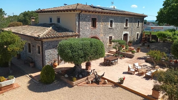 Un edificio de piedra con techo de tejas, un patio con asientos al aire libre y un árbol grande.
