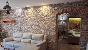 Un salón con paredes de piedra, un sofá color crema, un colgante de luz y una chimenea de piedra.