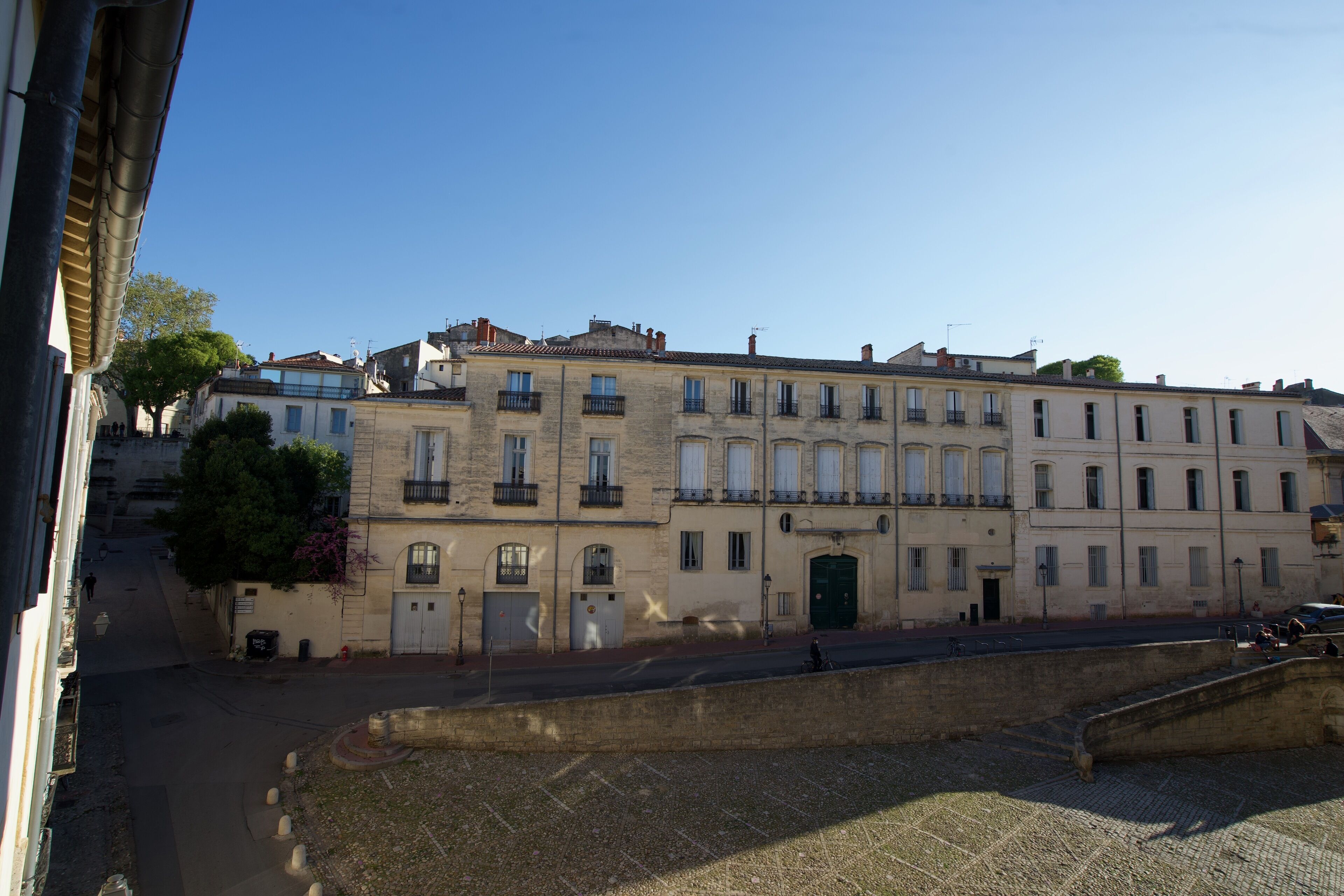 Une rangée de bâtiments historiques à l’architecture homogène, une rue pavée et une petite place.