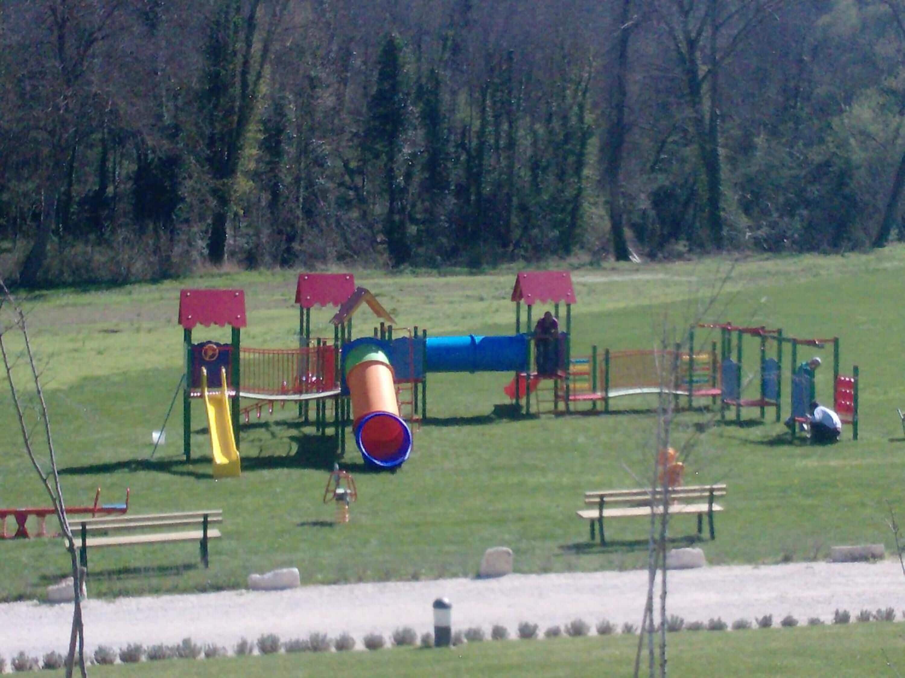 A playground with various play structures, including slides and climbing areas, surrounded by benches and trees.