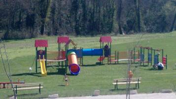 A playground with various play structures, including slides and climbing areas, surrounded by benches and trees.
