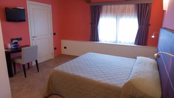 A bedroom with a bed, a desk, a chair, a television on the wall, and a window with curtains.