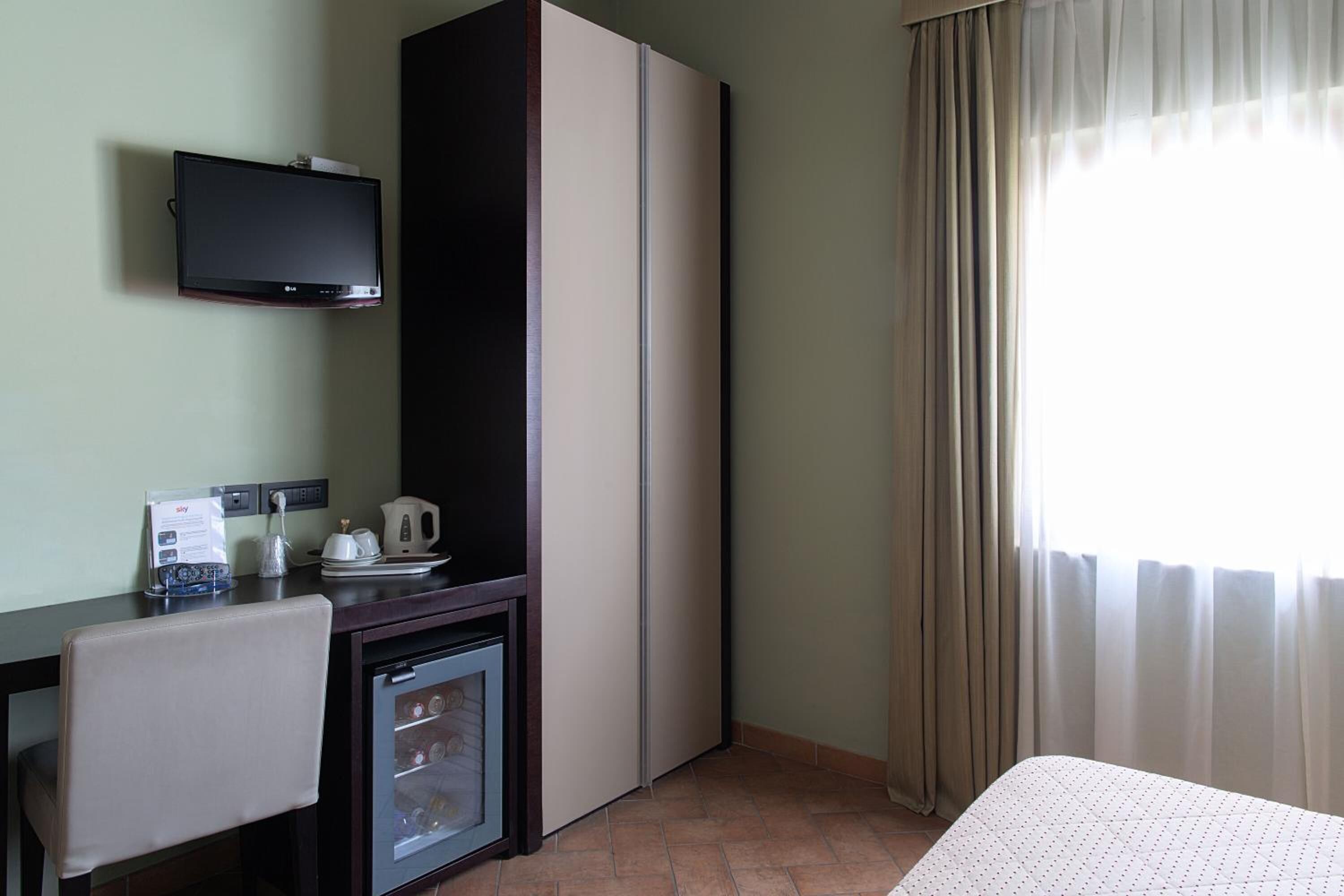 Une chambre d’hôtel comprenant un lit, un bureau avec une télévision, un minibar et une fenêtre avec des rideaux.