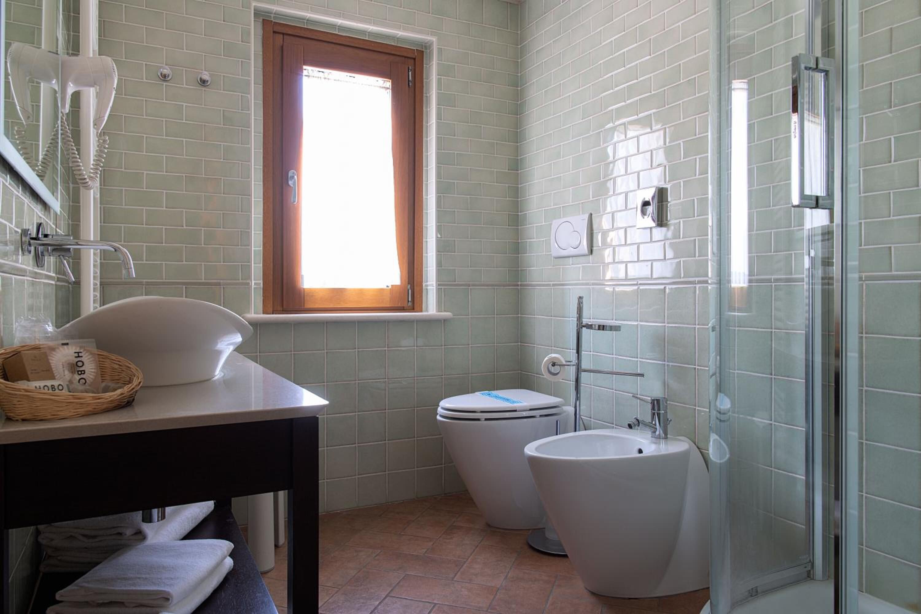 A bathroom with a sink, two toilets, a shower, and a window.