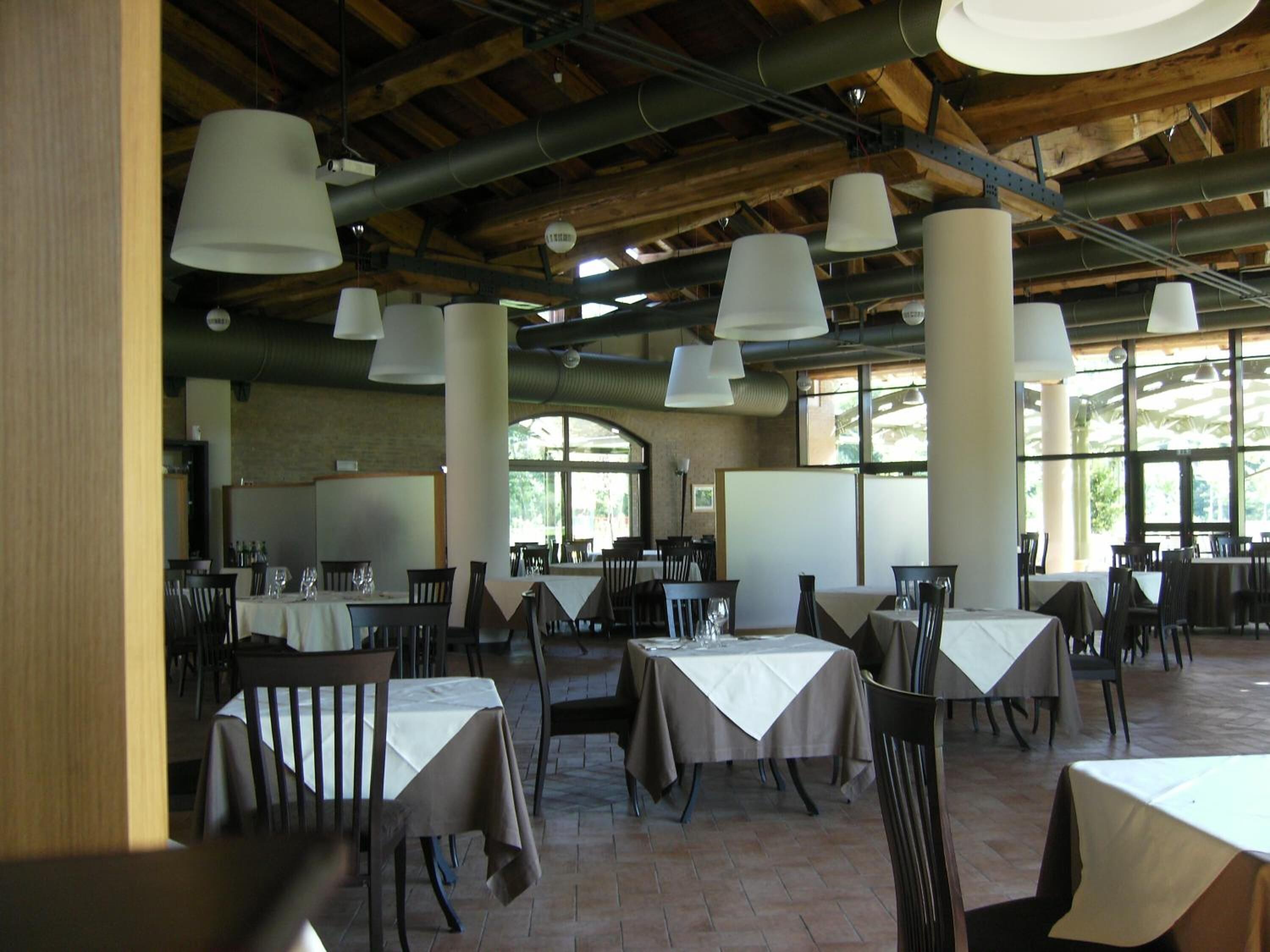 An indoor dining area with tables and chairs, large hanging lights, and a rustic wooden ceiling.