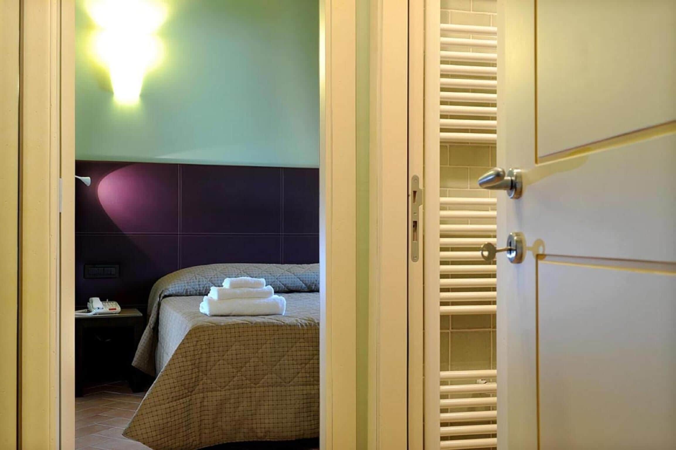 Une chambre d’hôtel avec un lit, une table de chevet avec un téléphone et un luminaire fixé au mur.