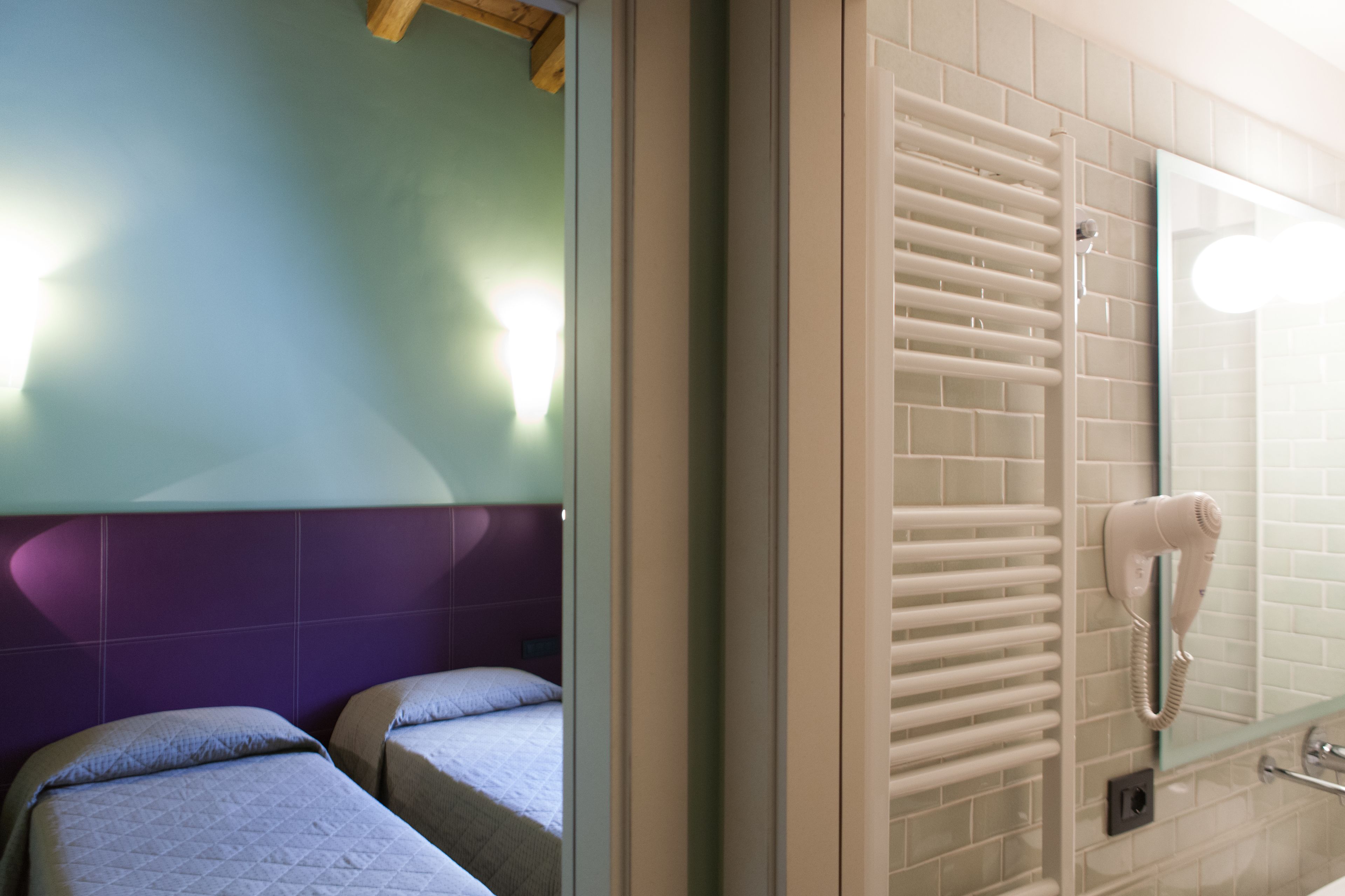 A hotel room with two beds, a bathroom with a towel rail and a hairdryer, and a mirror on the wall.