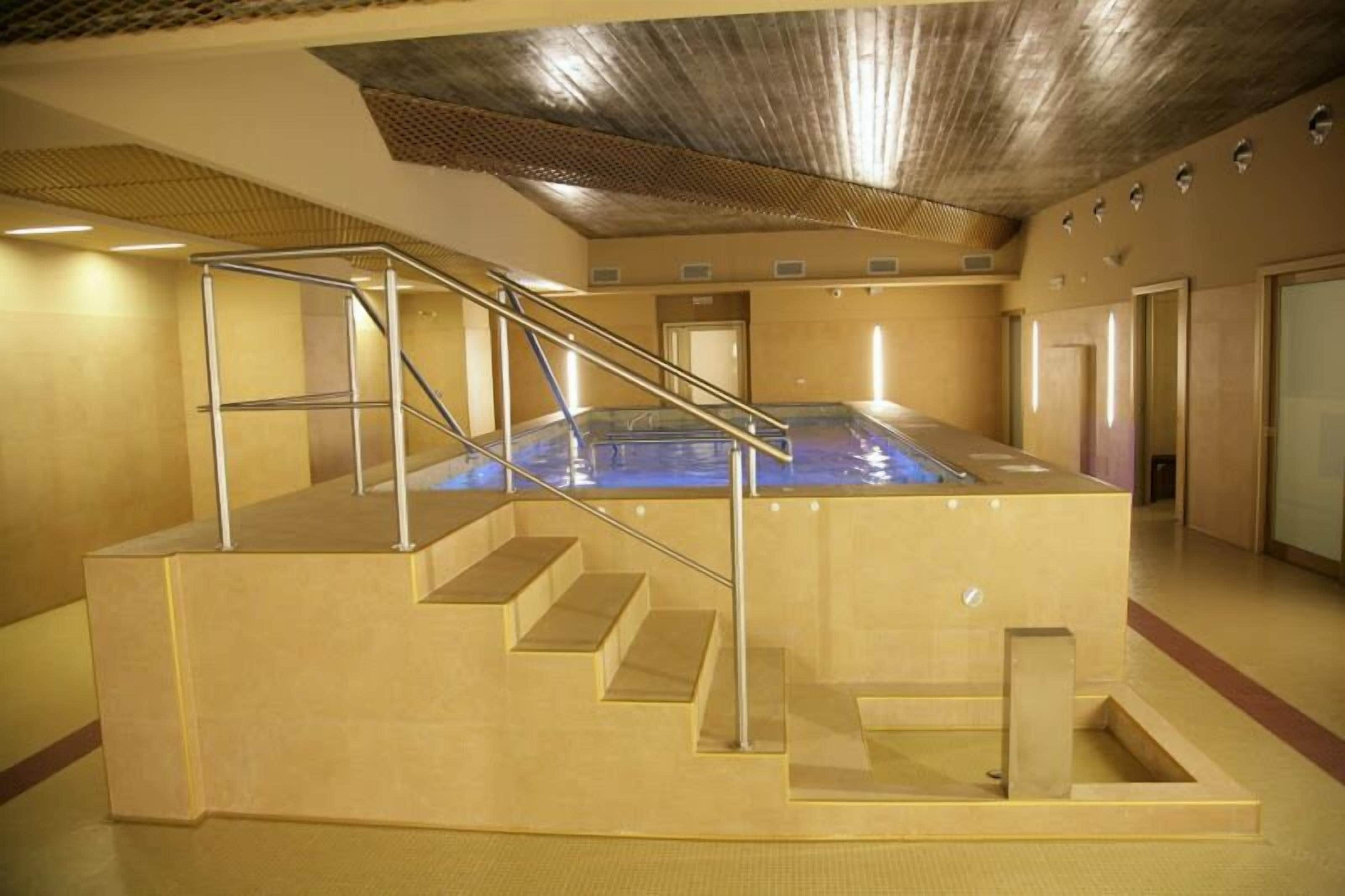 A large indoor swimming pool with a staircase leading up to it, surrounded by walls and a ceiling with a textured pattern.