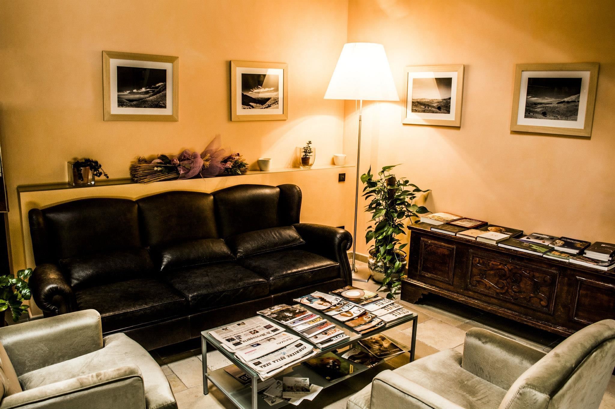 Una sala de estar con un sofá de cuero negro, una mesa de centro de vidrio con revistas, una lámpara y un mueble de madera con marcos de fotos.