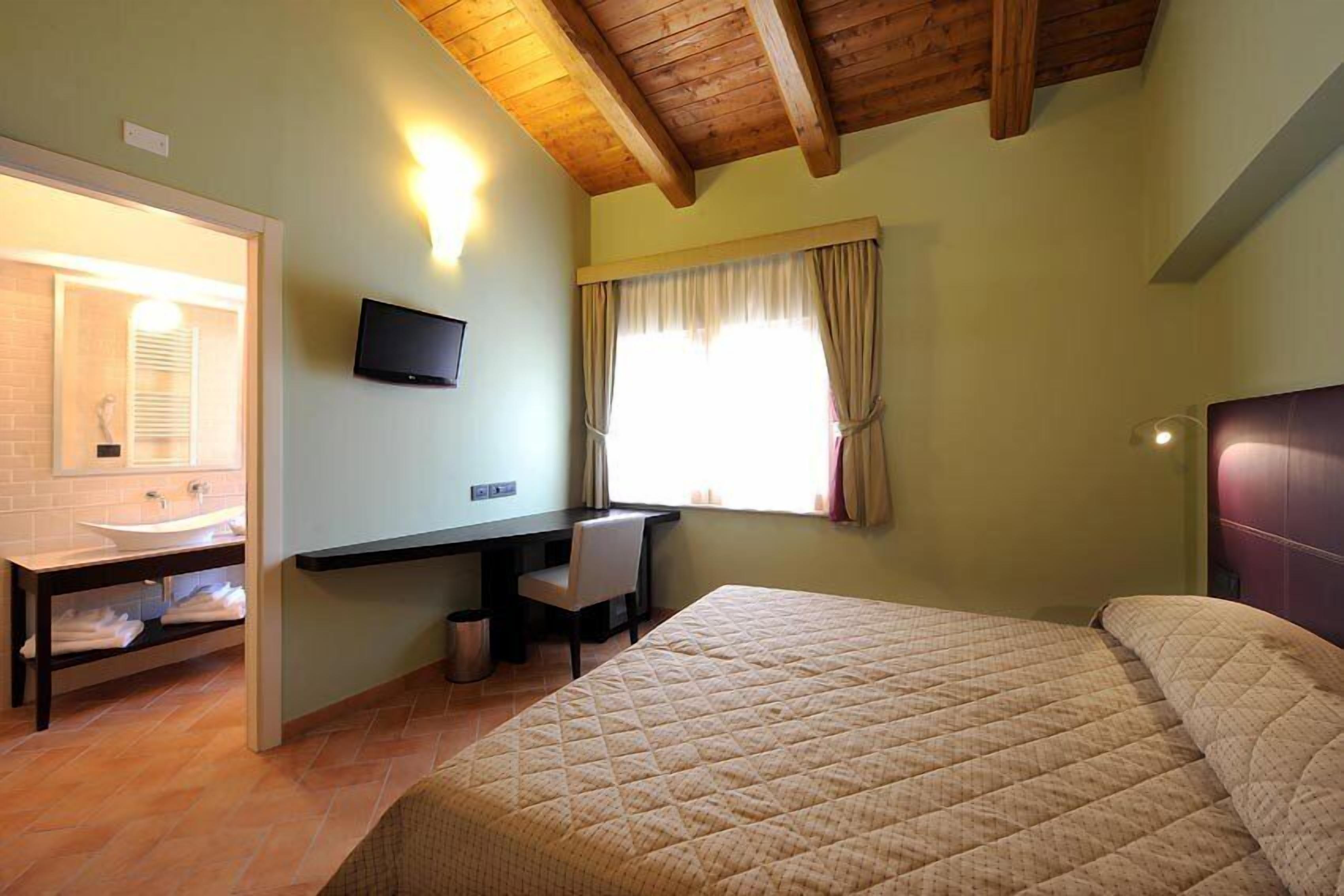A bedroom with a bed, a desk, a chair, a TV, and a window with curtains.