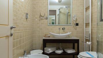 Un baño con paredes de azulejos color beige, un lavabo blanco, un espejo, un inodoro y una zona de ducha.
