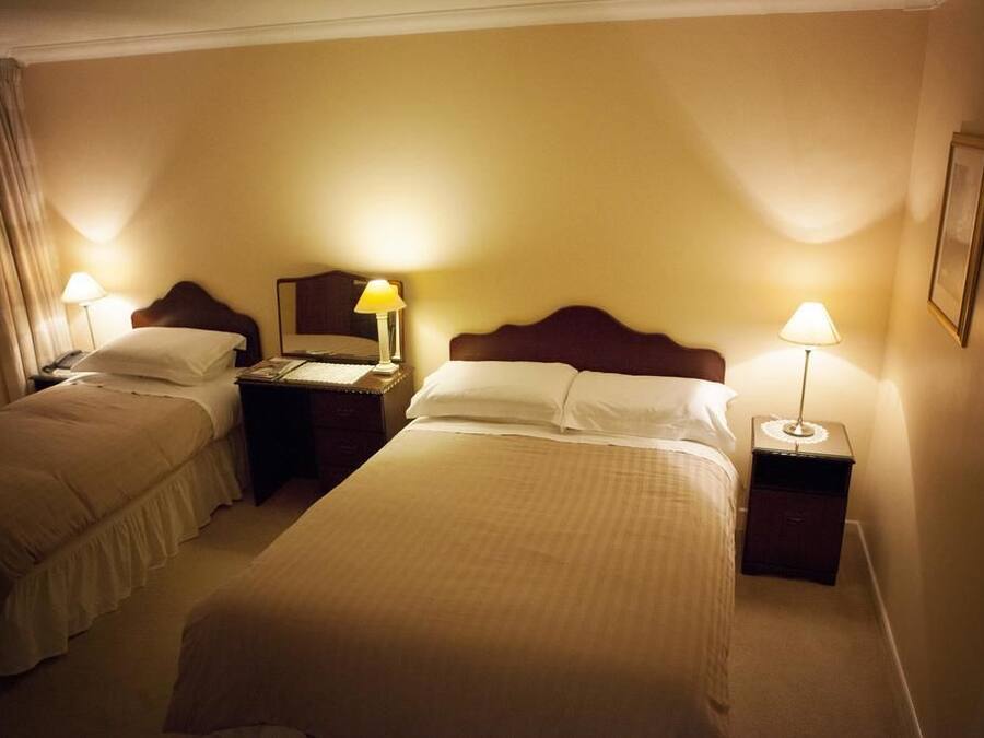 Habitación de hotel con dos camas individuales, mesitas de noche con lámparas y un pequeño escritorio con teléfono.
