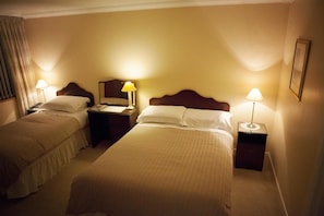 A hotel room with two single beds, bedside tables with lamps, and a nightstand with a telephone.