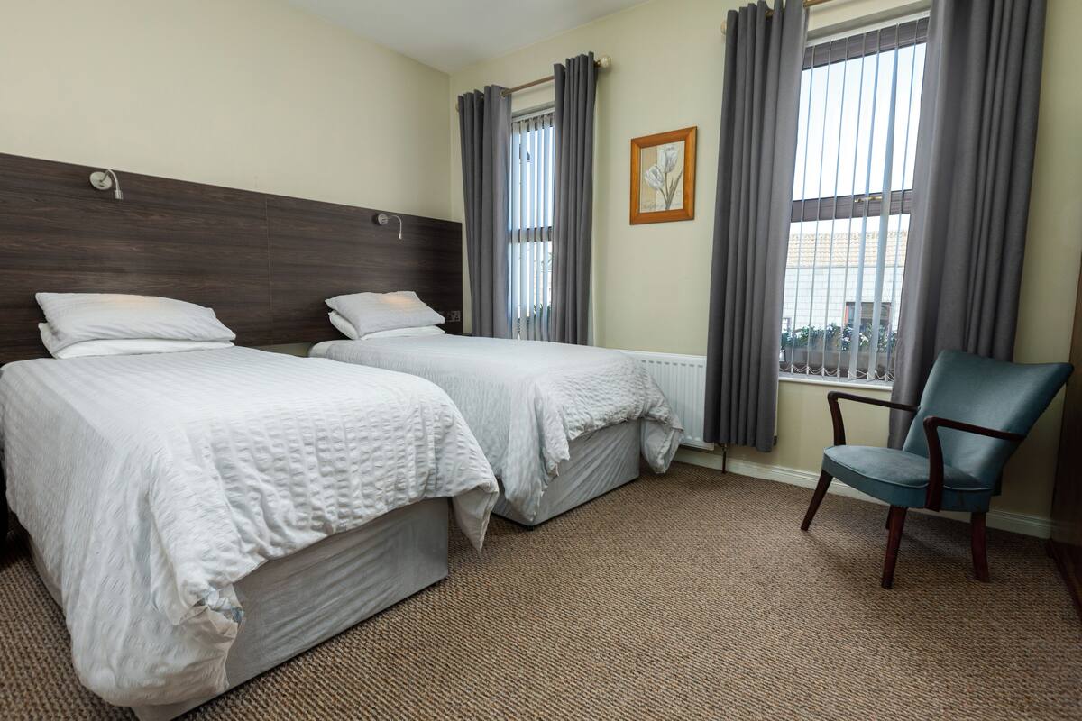 A hotel room with two beds, a chair, and a window with curtains.