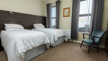 A hotel room with two beds, a chair, and a window with curtains.