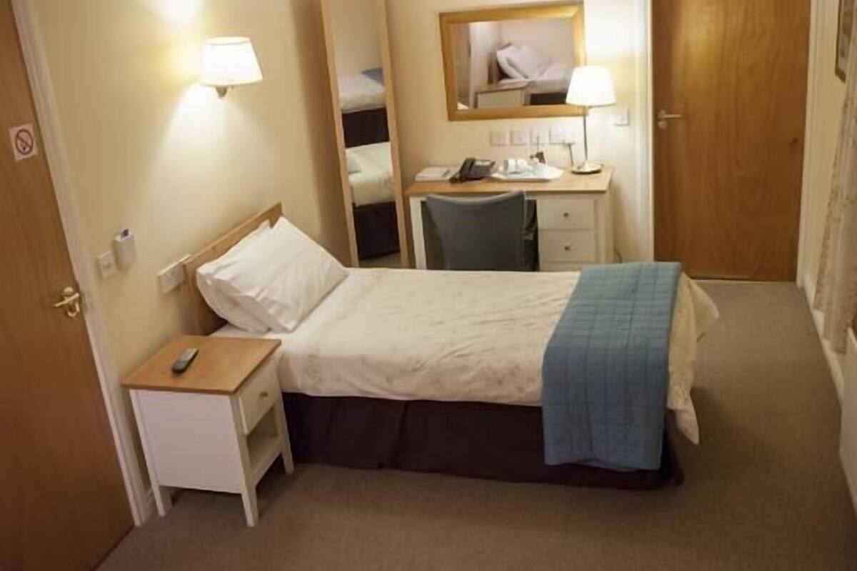 A hotel room with a bed, bedside table, lamp, desk, chair, and a wardrobe.