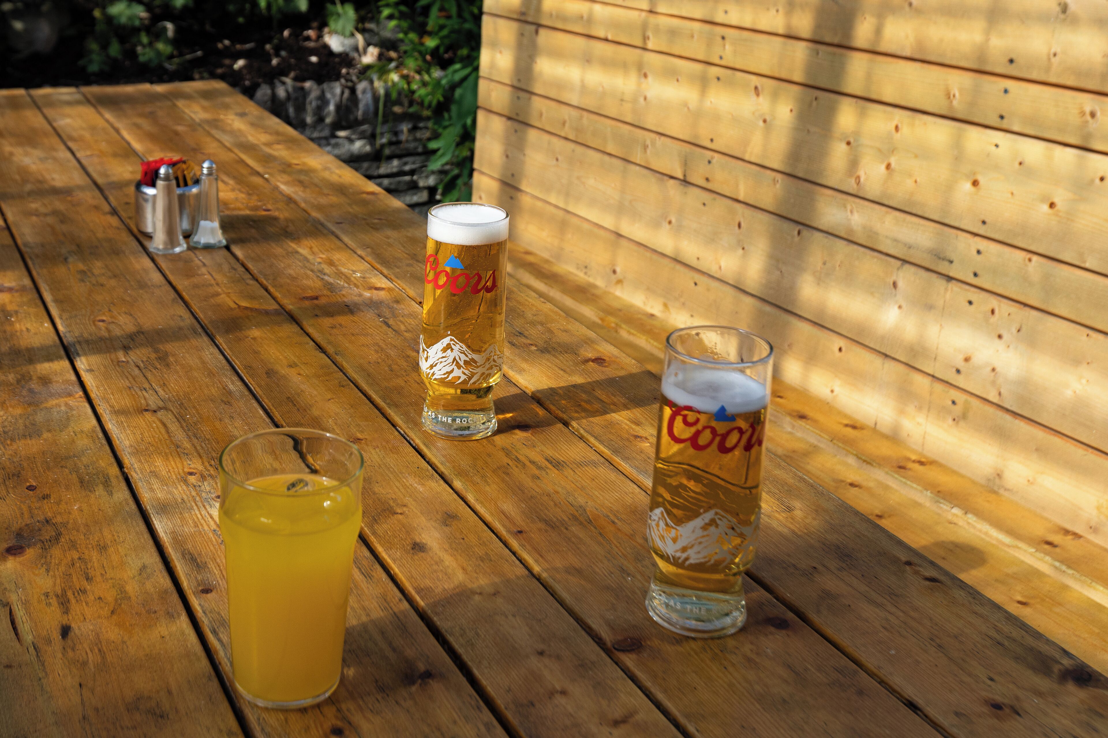 Una mesa de madera con tres vasos de cerveza y un vaso de zumo de naranja.