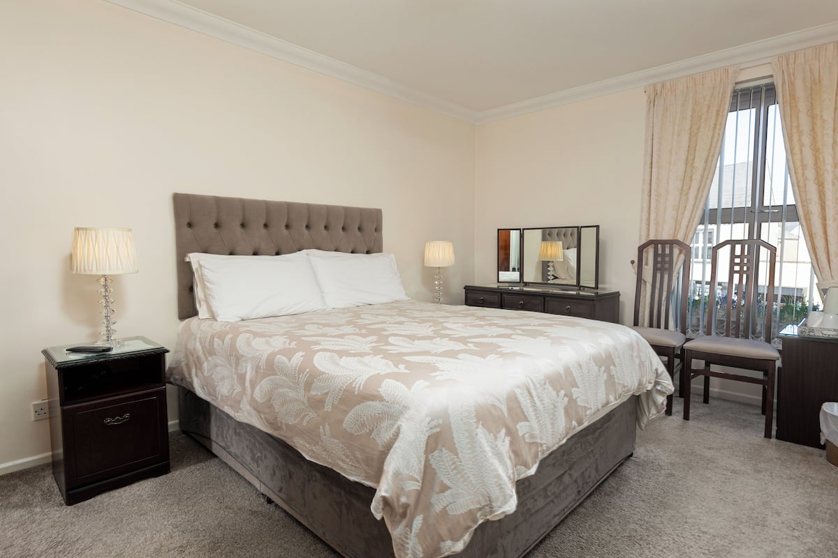A neatly arranged bedroom with a large bed, bedside tables, a mirror, and a chair.