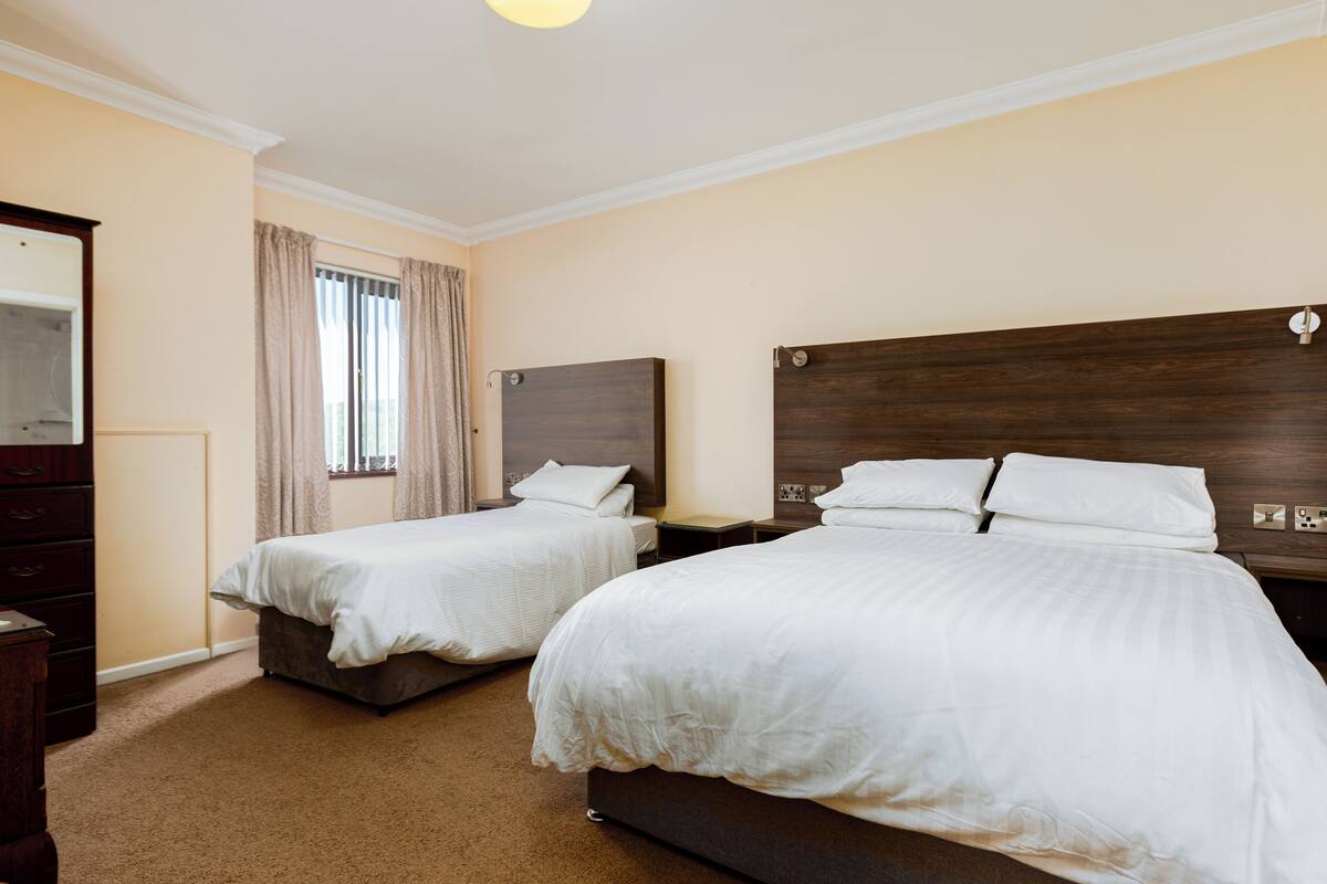A hotel room with two single beds, a dresser, and a window with curtains.