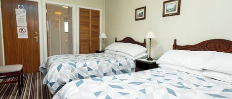 A hotel room with two beds, a bench, a door, and two framed pictures on the wall.