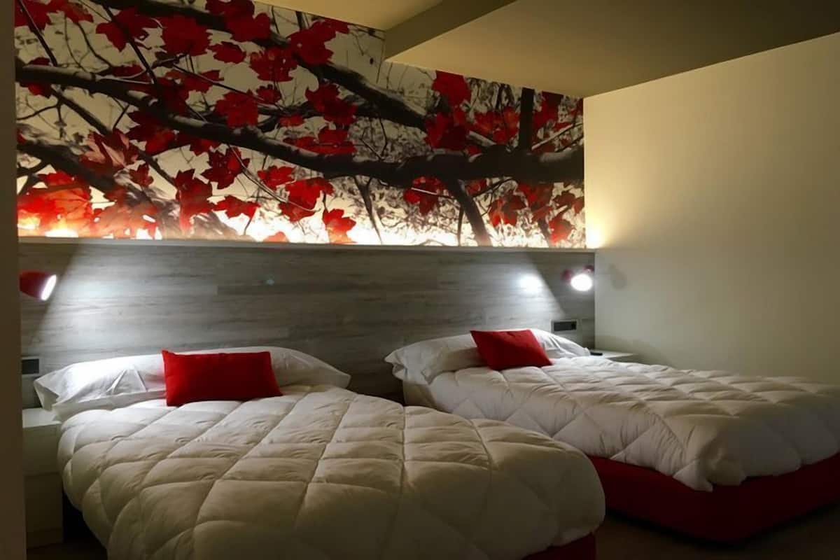 A hotel room with two beds, each with a red pillow, and a wall mural of red leaves on a tree.