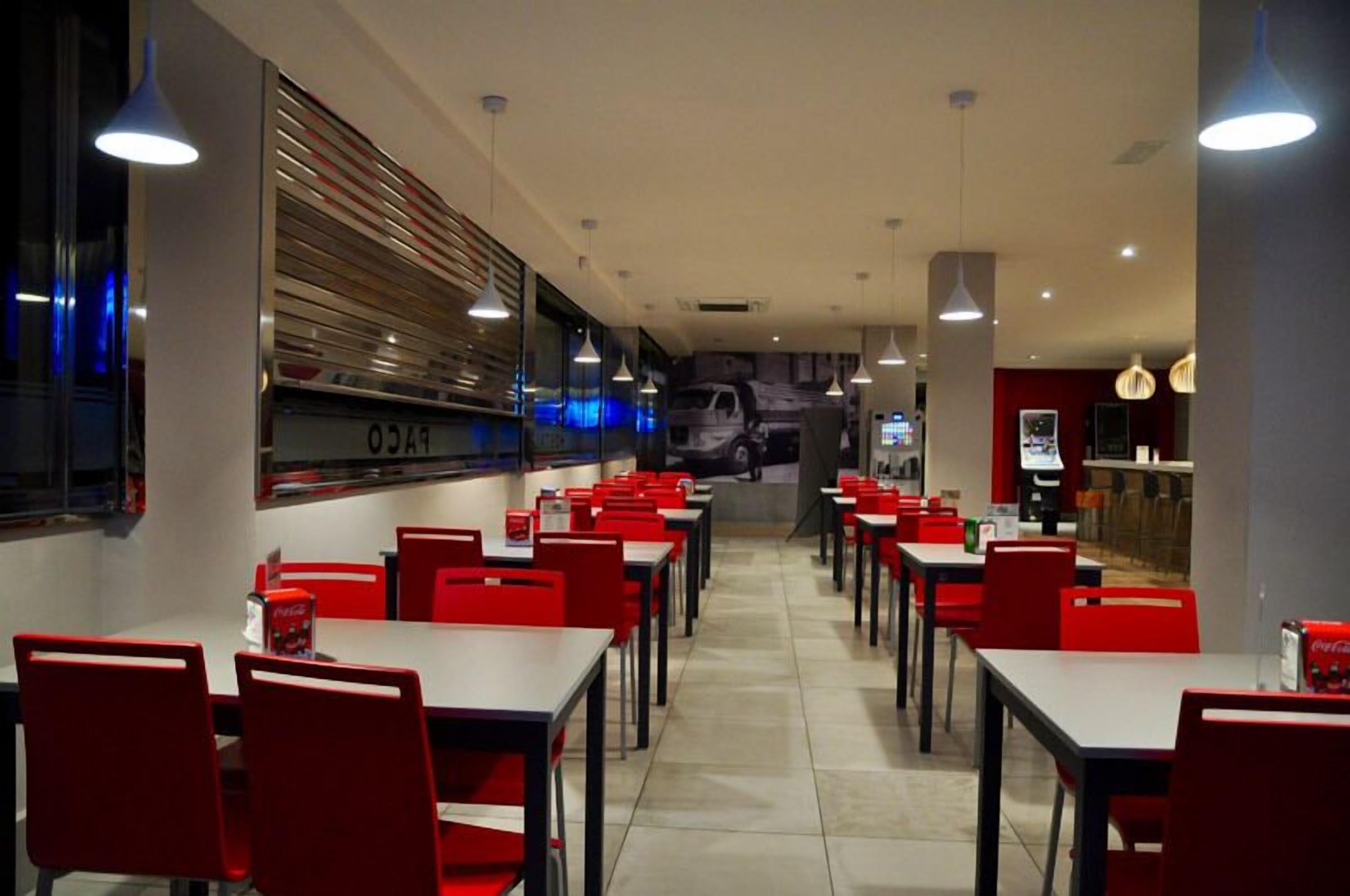 A restaurant with red chairs and tables, a counter with a menu, and a wall with a vehicle image.