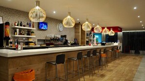 Zona de bar moderna con mostrador de madera, varios taburetes y lámparas colgantes.