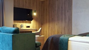 Quarto de hotel com sofá, cama, escrivaninha, televisão de tela plana e parede de destaque em madeira.