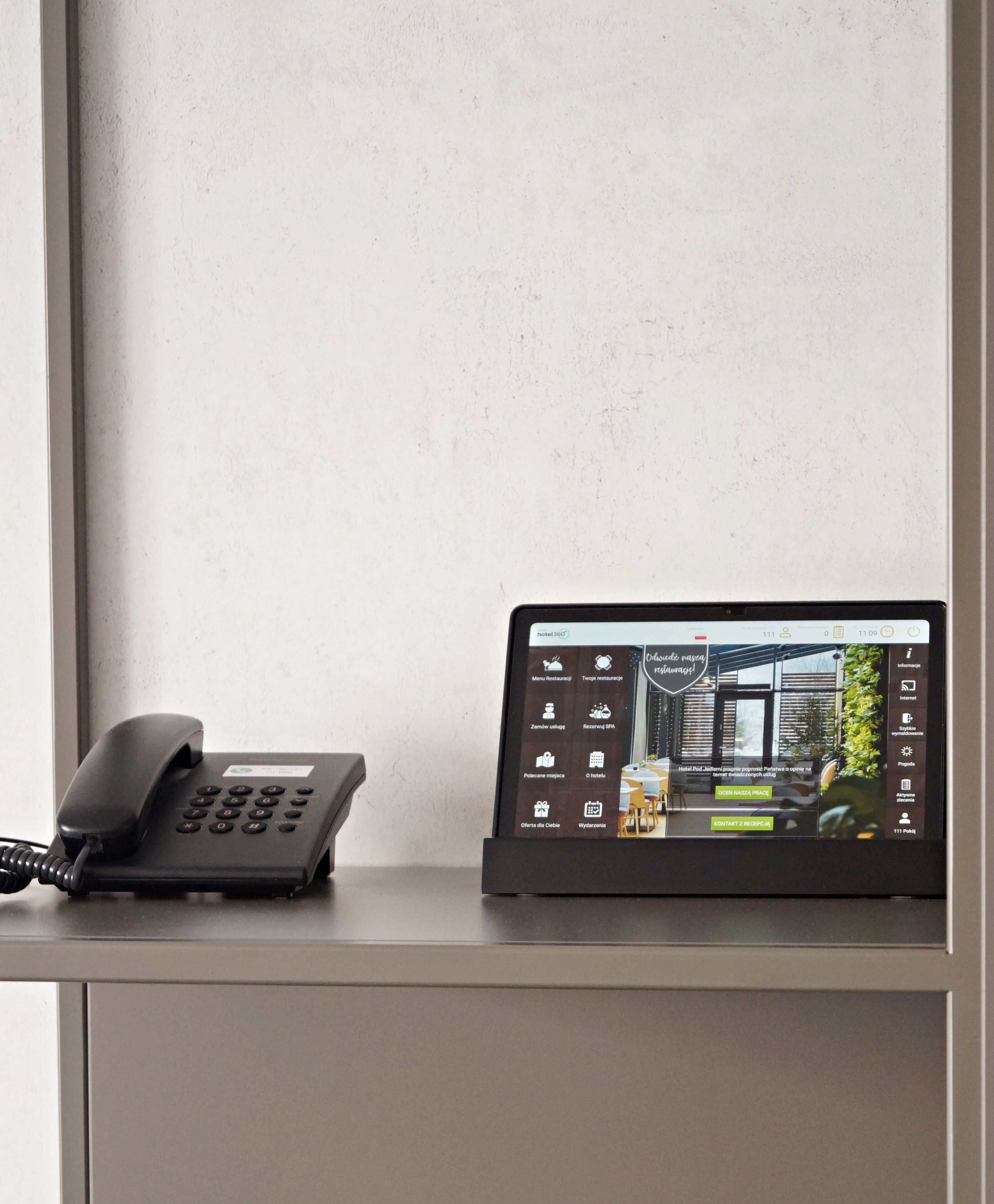 Mostrador de recepción de un hotel con un teléfono tradicional y una pantalla digital que muestra la página web del hotel.