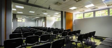 A conference room with rows of chairs, a projector, and windows with a view of greenery.